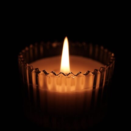 A single candle flame glowing warmly against a dark background.