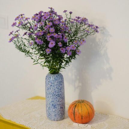 Purple asters in a blue vase, with a small pumpkin, create a charming rustic decor.